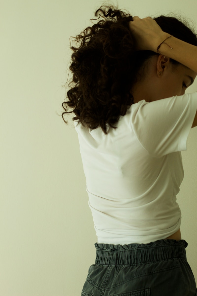 a woman in a white shirt is holding her hair